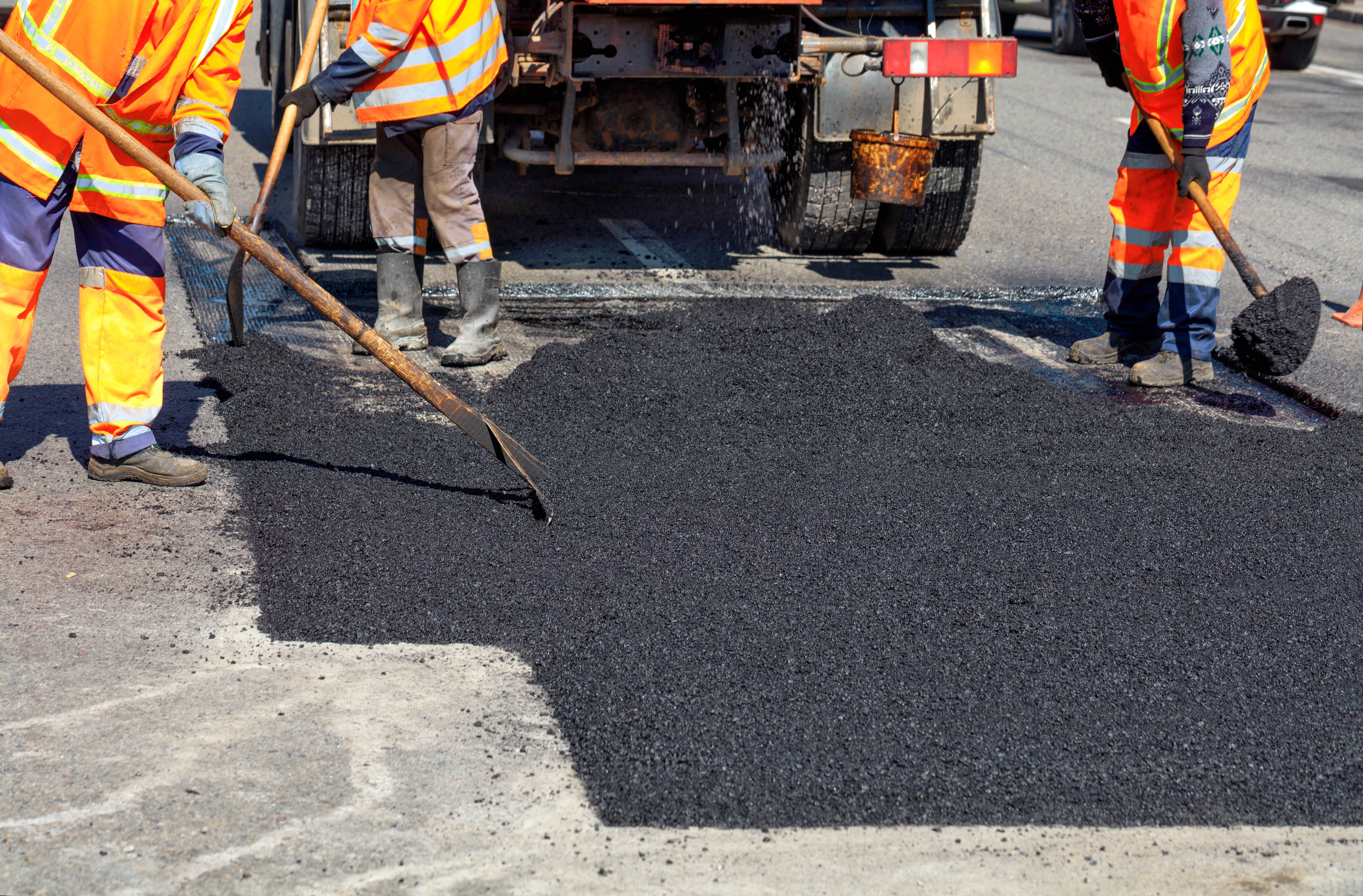 Road workers are shoveling asphalt to repair the pavement.